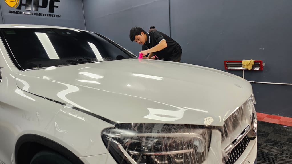 ช่างกำลังรีดแผ่นฟิล์มใสกันรอยบนหลังคารถ SUV สีขาว ฝากระโปรงและไฟหน้าคลุมด้วยแผ่นฟิล์มเปียกไว้แล้ว งานติดฟิล์ม PPF ร้านบ้านน้ำอิง ออโต้สปา บางสะพาน