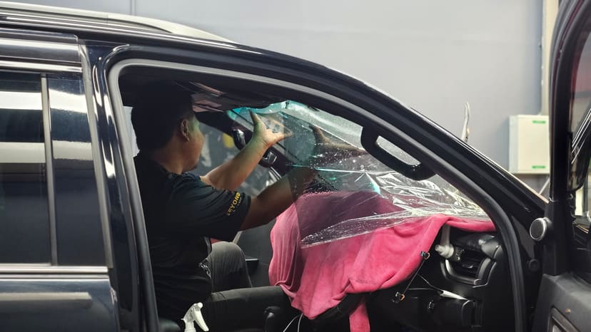 ช่างกำลังติดฟิล์มกรองแสงกระจกหน้า Toyota Fortuner สีดำ